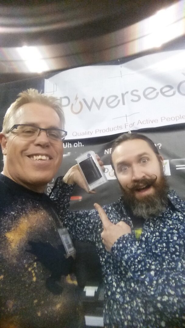 Here's an alt tag for the image: Two men at Powerseed booth, showing product.